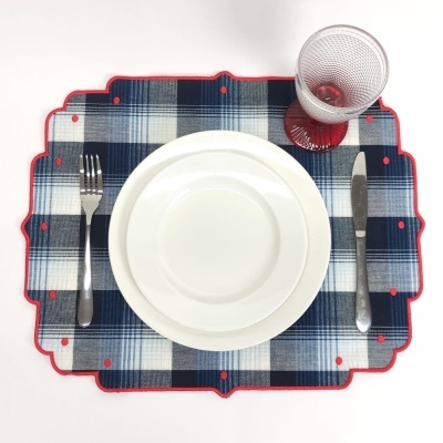 Jogo americano xadrez azul com prato branco, talheres metálicos e copo de vidro com base vermelha