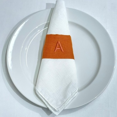 Prato branco com guardanapo branco preso por anel de tecido laranja com letra A