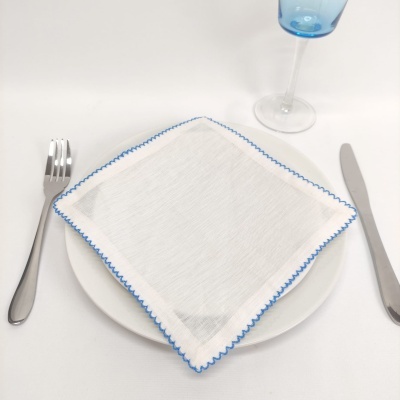 Conjunto de mesa com prato branco, guardanapo branco com borda azul, talheres e copo azul