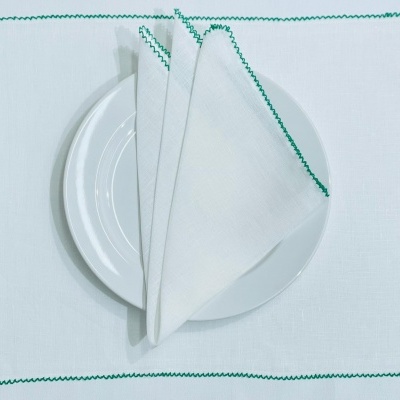 Jogo americano e guardanapo brancos com bordas verdes e prato branco no centro