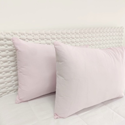 Dois almofadões roxos claros num colchão branco com cabeceira trançada branca