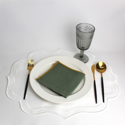 Conjunto de louça e talheres com guardanapo verde e copo transparente sobre base branca ondulada