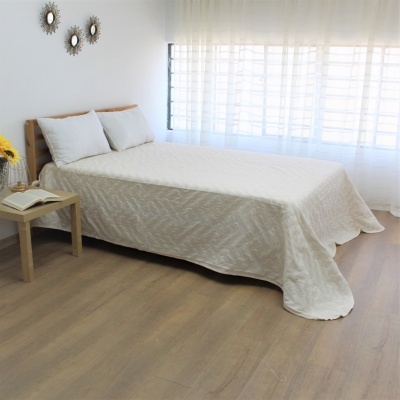 Cama de casal com colcha branca e almofadas, mesa de cabeceira com flores e livro, ambiente claro e minimalista