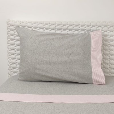 Travesseiro com fronha cinzenta e borda rosa, cama com base cinzenta e cabeceira branca acolchoada