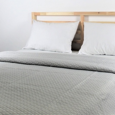 Cama de casal com almofadas brancas e colcha cinza matelassada.