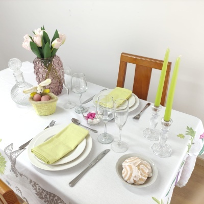 Mesa posta com pratos, copos, talheres, jarra com flores e decorações de páscoa