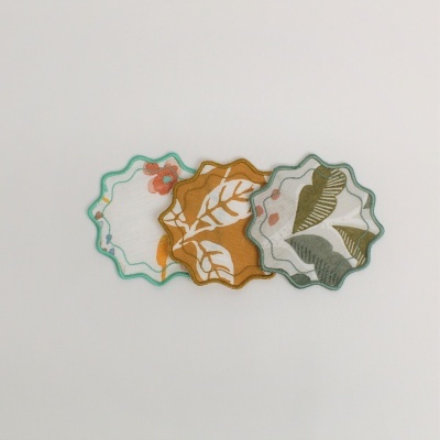 Três bases para copos em tecido com estampas de folhas e flores, moldura ondulada