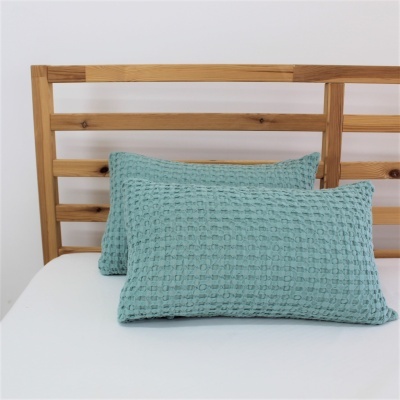 Duas almofadas azuis turquesa com textura waffle numa cama de madeira clara