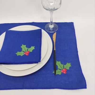 Conjunto de mesa azul com decoração de folhas verdes e bagas vermelhas, prato branco, faca dourada e copo de vidro