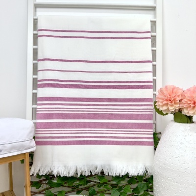 Manta ou toalha branca com riscas rosas pendurada, cadeira com almofada branca à esquerda e vaso com flores rosas à direita