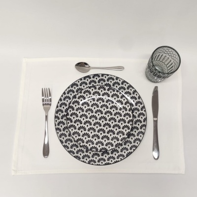 Prato branco com padrão preto, talheres metálicos e copo de vidro listrado em mesa branca