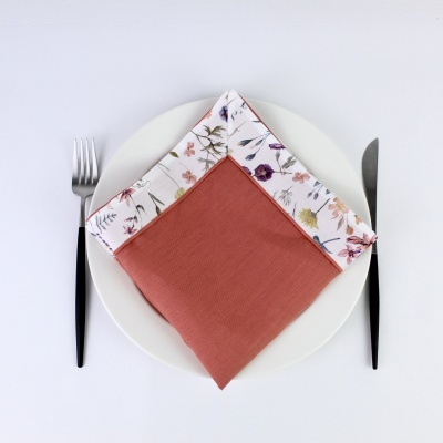 Guardanapo bicolor tecido num prato branco com talheres pretos ao lado