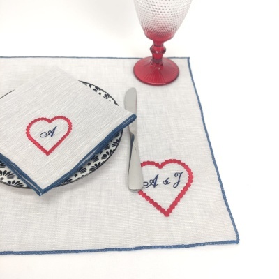 Jogo americano e guardanapo brancos bordados com coração e letras, copo vermelho e prato com padrão preto e branco