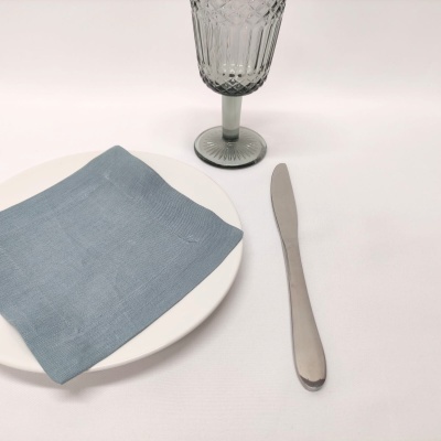 Mesa posta com prato branco, guardanapo azul, faca de metal e copo de vidro