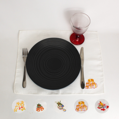 Conjunto de mesa com prato preto, guardanapo branco bordado, talheres metálicos e copo vermelho texturizado