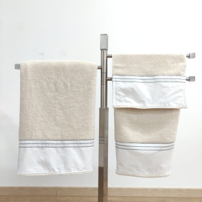 Conjunto de toalhas bege com acabamento branco penduradas num suporte metálico