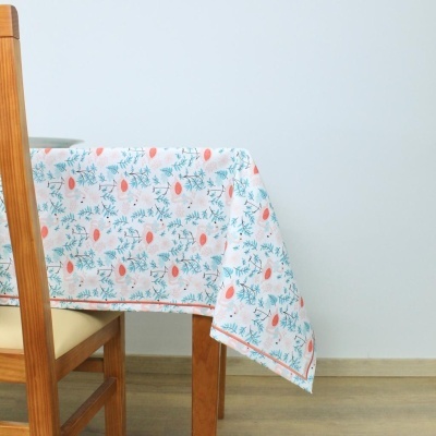 Toalha de mesa branca com padrão floral em tons de coral e verde sobre mesa de madeira num ambiente interior