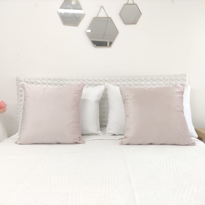 Cama com almofadas cor-de-rosa e branca, cabeceira branca texturizada e três espelhos hexagonais na parede.