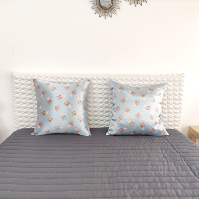 Duas almofadas azuis com flores num quarto com cama e cabeceira branca