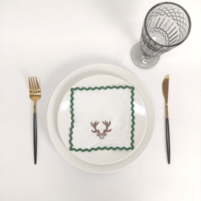 Conjunto de jantar com prato branco, guardanapo decorado, talheres dourados e copo transparente