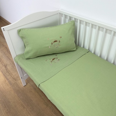 Cama de bebé branca com roupa de cama verde clara e bordados pequenos