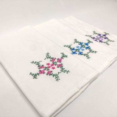 Três toalhas brancas bordadas com flores em rosa, azul e roxo