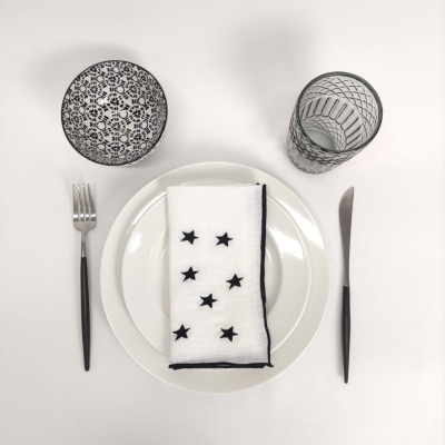 Conjunto de loiça com prato branco, guardanapo com estrelas, talheres pretos e copos decorativos