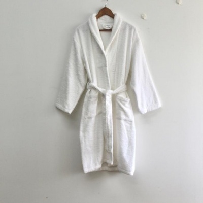 Roupão branco felpudo com cinto pendurado na parede branca