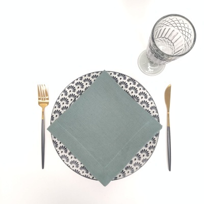 Conjunto de prato com guardanapo verde, talheres pretos e dourados e copo de vidro transparente