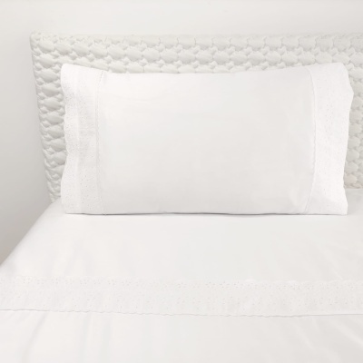 Almofada branca com bordado inglês e lençol branco com faixa bordada num ambiente neutro