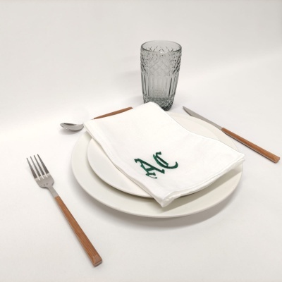 Mesa posta com prato branco, guardanapo bordado, talheres com cabo de madeira e copo de vidro texturizado