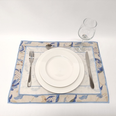 Conjunto de mesa com pratos brancos e talheres sobre toalha padrão azul e bege.