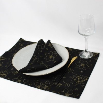 Conjunto de guardanapo e toalhete em tecido preto com padrão dourado, prato branco e copo de vidro