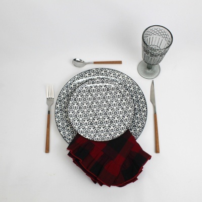 Conjunto de louça com pratos decorados, talheres com cabo de madeira, copo de vidro e guardanapo xadrez vermelho e preto