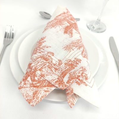Guardanapo branco com padrão castanho avermelhado sobre prato branco e talheres