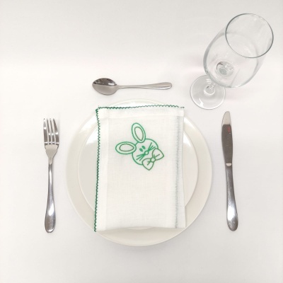 Mesa posta com talheres, prato branco, guardanapo com bordado de coelho e copo de vidro