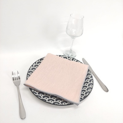 Mesa posta com prato com padrão floral, guardanapo rosa, talheres de metal e copo de vidro.