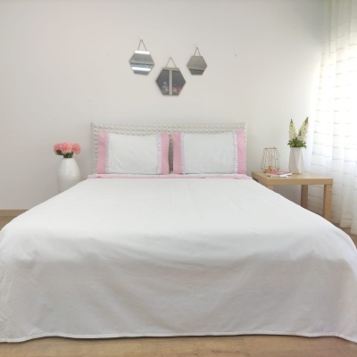 Cama com roupa branca e bordas cor-de-rosa, espelhos hexagonais e decoração minimalista