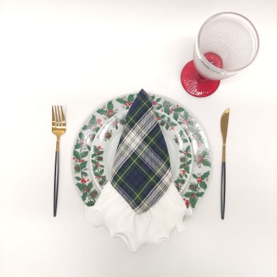Conjunto de mesa com pratos decorados, guardanapo xadrez, talheres dourados e copo transparente com base vermelha.
