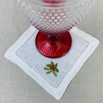 Guardanapo branco com bordado de folhagem e bagas sob copo de vidro com base vermelha