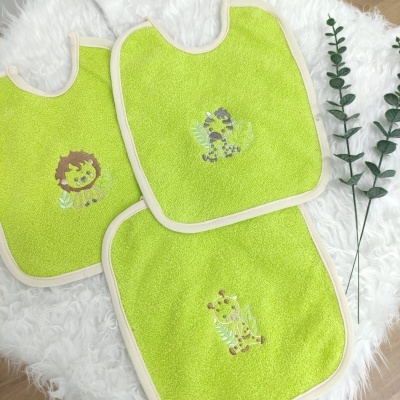 Três babetes verdes com bordados de animais sobre tecido branco felpudo