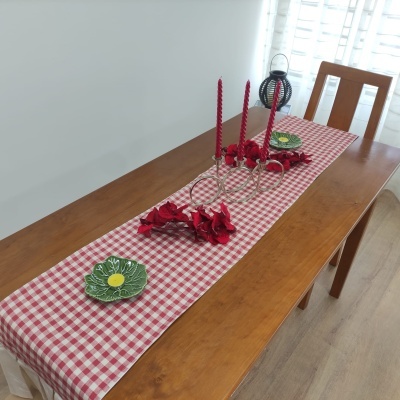 Caminho de mesa xadrez vermelho e branco com decoração de velas e flores sobre mesa de madeira.