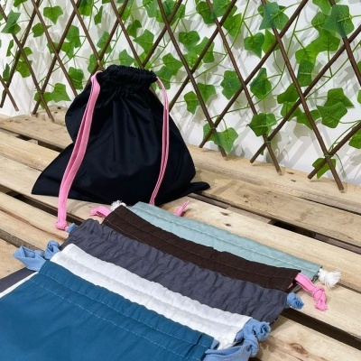 Saquinhos de tecido coloridos com cordões em superfície de madeira e fundo com treliça e folhas verdes