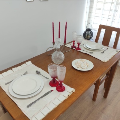 Mesa de jantar com pratos brancos, copos vermelhos, castiçal com velas vermelhas e doce sobre toalhas brancas.