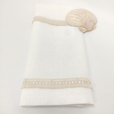 Guardanapo branco com bordas bege e concha decorativa no canto.