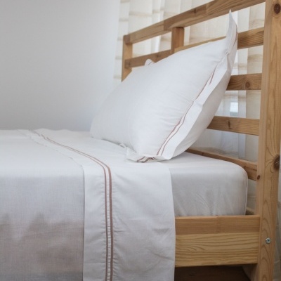 Cama de madeira clara com lençóis brancos e linhas decorativas bege