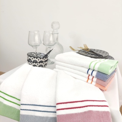 Toalhas brancas com riscas coloridas, louça preta e branca, copos e garrafa de vidro, pratos cinza e talheres dourados num ambiente minimalista