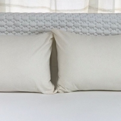 Cabeceira cinza trançada com almofadas brancas e lençol branco numa cama