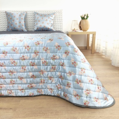 Cobertura de cama azul claro com padrão floral rosa sob cama com almofadas.