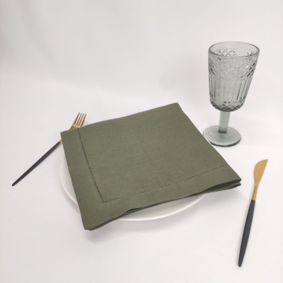 Conjunto de jantar com prato branco, guardanapo verde, talheres com cabos pretos e dourados, e copo de vidro decorado